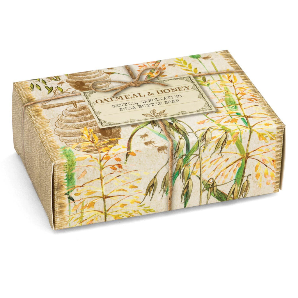 Oatmeal & Honey bar of soap in a cardboard gift box.  Box is printed with an artistic scene of bee hives, wheat, trees, and twine.  The label reads 'Oatmeal & Honey Gentle Exfoliating Shea Butter Soap"