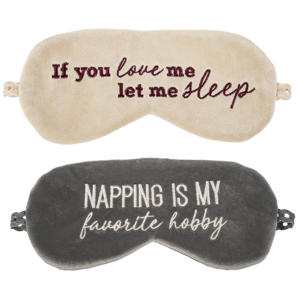 Two velvet sleeping masks on a white background.  The one on top is off white with embroidered maroon text that says 'If you love me let me sleep.'  The mask on bottom is gray with off white embroidered text that says 'Napping is my favorite hobby'