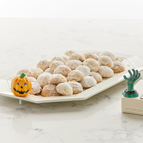 A photo of an octagonal tray filled with melt-a-way cookies.  At the end of the tray is a ceramic jack o lantern that is attached to the tray via a small hole.  On the right is a corner of another tray with an attachment of a creepy green hand coming out of the ground.