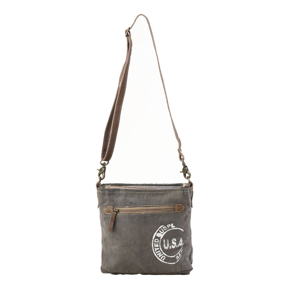 The back of a shoulder bag, the canvas is dark gray and features a large round printed stamp graphic that says 'U.S.A.' in the middle.