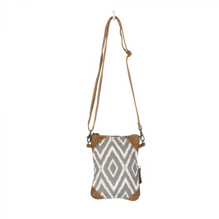 Rectangular cross body bag with a gray and off white diamond pattern, and brown leather triangular details in each of the 4 corners.  The bag is suspended by its thin brown strap from a white hook.