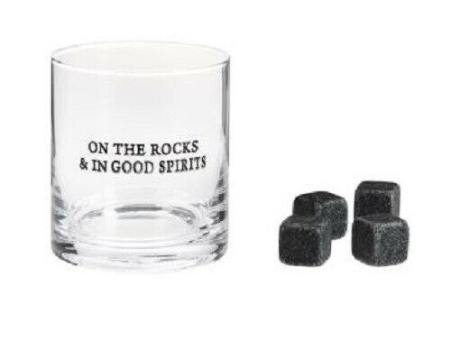 A clear rocks glass with black text on it that says 'On The Rocks & In Good Spirits'.  Next to it are 4 black stones.